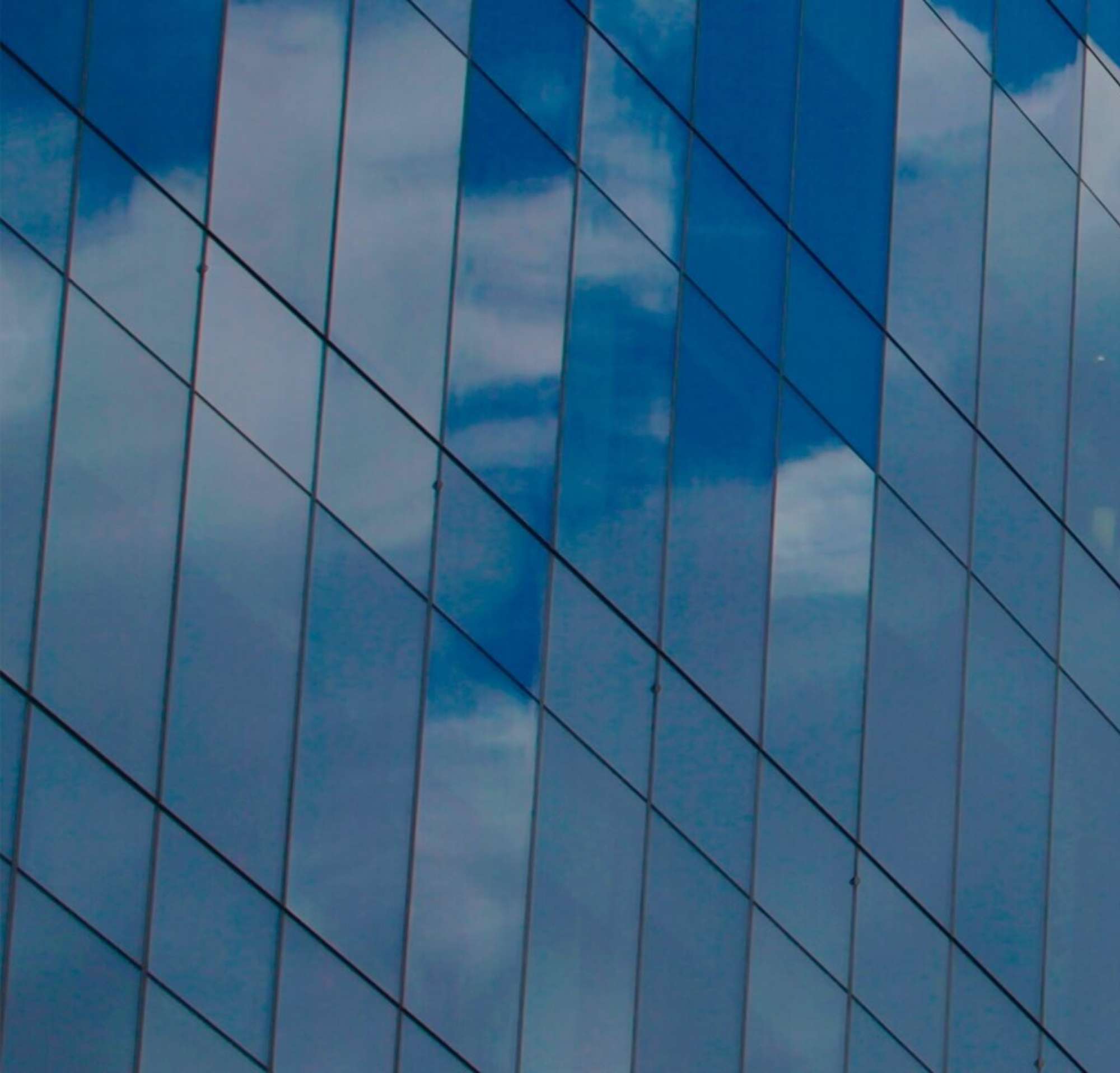 Glass windows on a high rise building, reflecting clouds.
